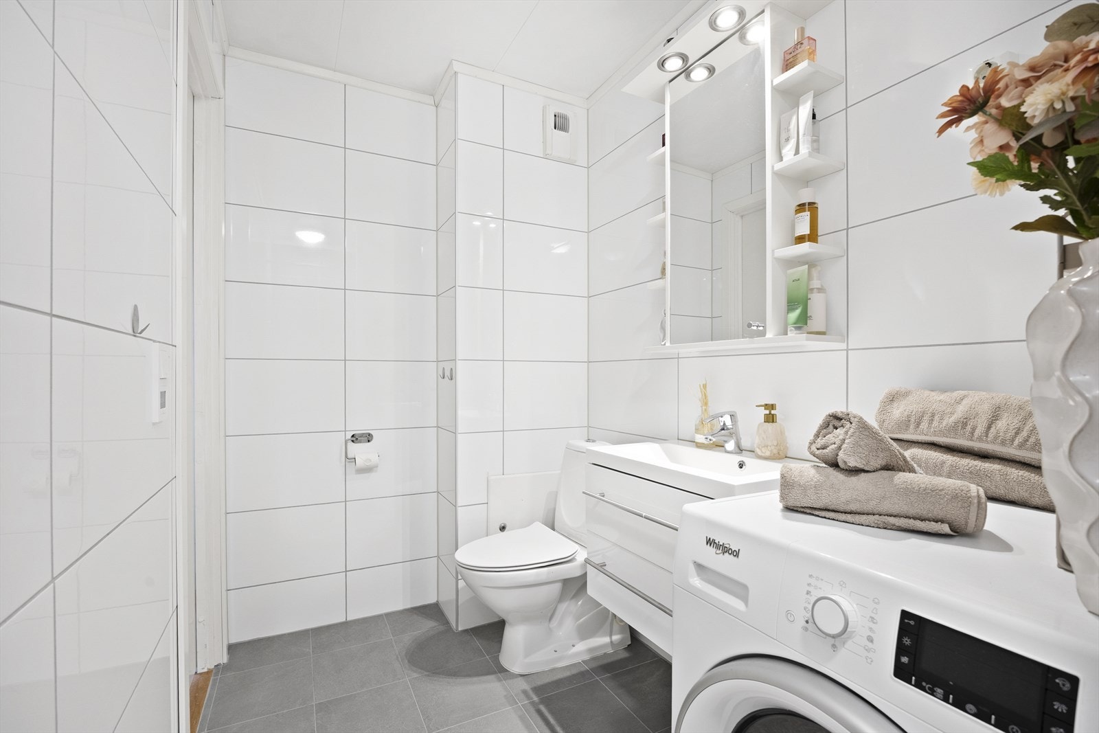 Baderomsinnredningen har hvite fronter og består av en heldekkende servant på en skuffeseksjon og et speilskap med hyller og belysning. Videre har badet et toalett, en dusjnisje og opplegg for vaskemaskin. Galleribilde
