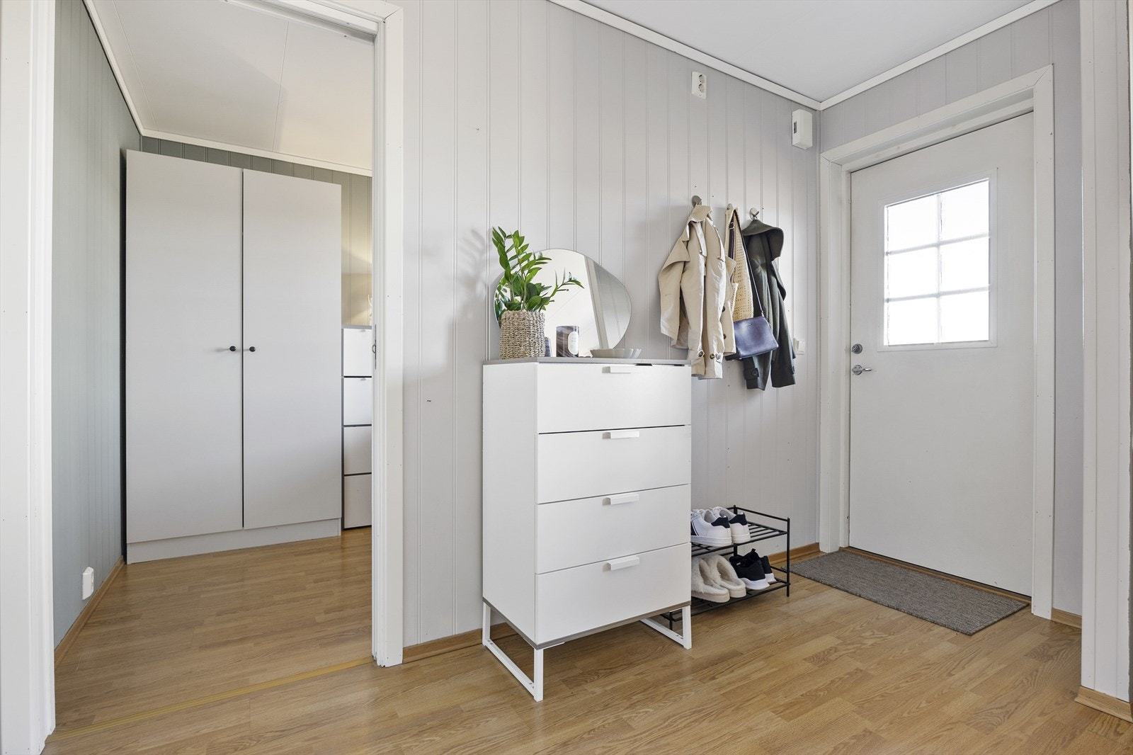 Vel inne blir vi ønsket velkommen i en fin entré med lysmalt panel på veggene og gyllen laminat på gulvet. Galleribilde