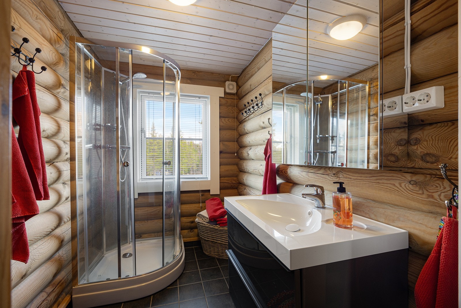 Badet fremstår som velholdt og pent, med liggende tømmervegger og koksgrå fliser på gulv med gulvvarme. Galleribilde