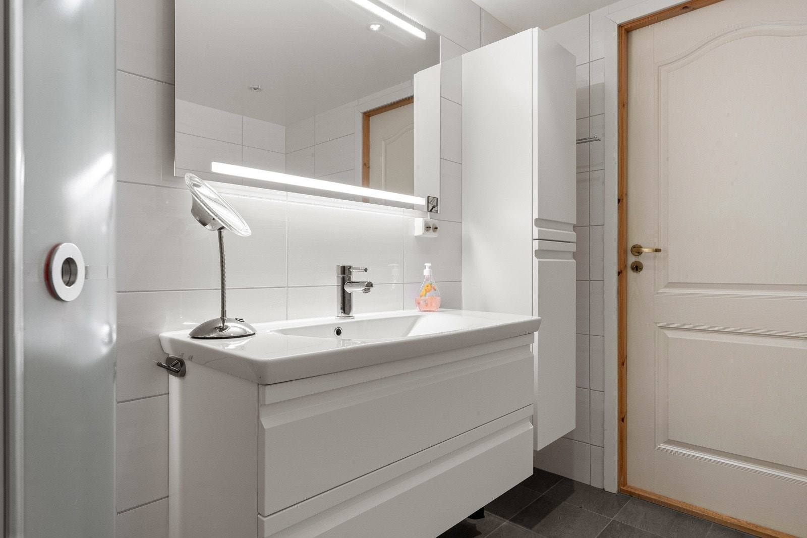 Moderne baderomsinnredning med skuffer, heldekkende servant, høyskap og speil med lys