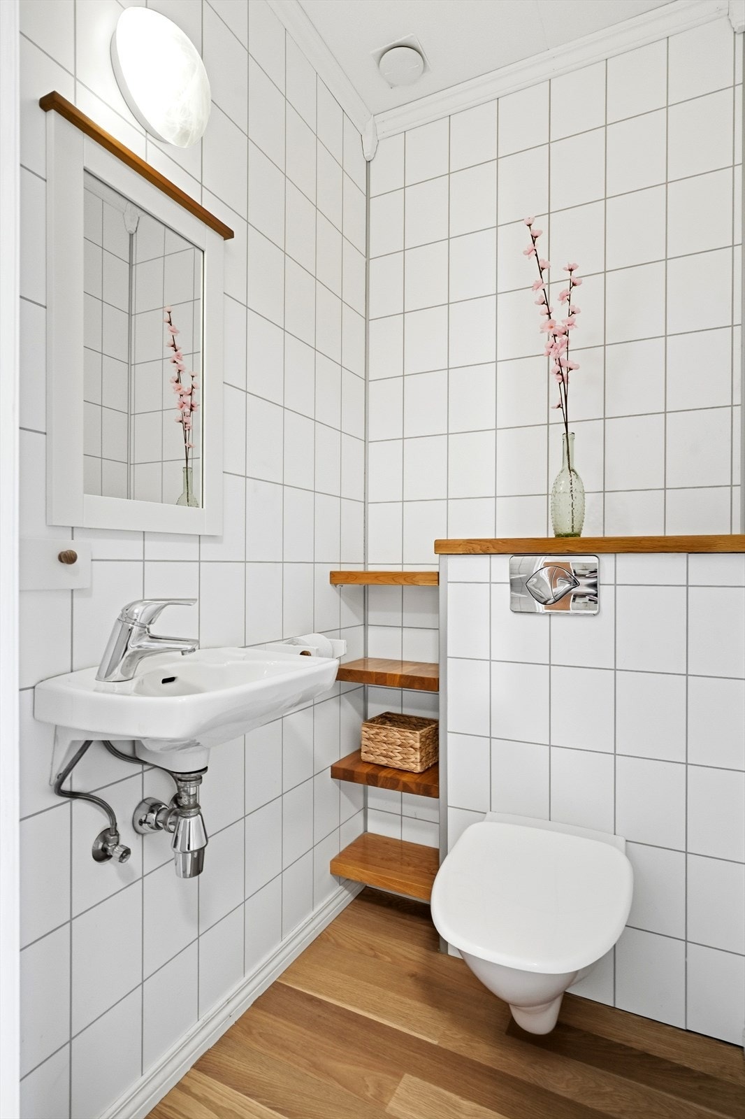Lyst toalettrom bestående av vask og klosett. Gulv er belagt med laminat, vegger er fliselagt og det er himlingsplater i tak. Galleribilde