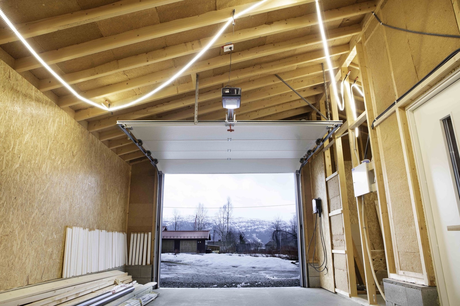 Romslig elektrisk garasjeport der du kan kjøre rett inn med SUV med takboks. Elbillader til høyre ved porten. Galleribilde