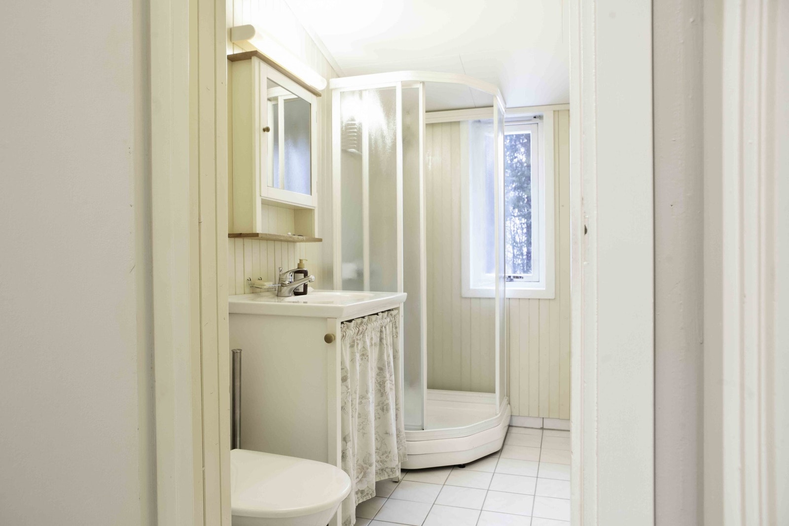 Lyst og sjarmerende bad med malt trepanel på veggene og fliser på gulvet. Galleribilde