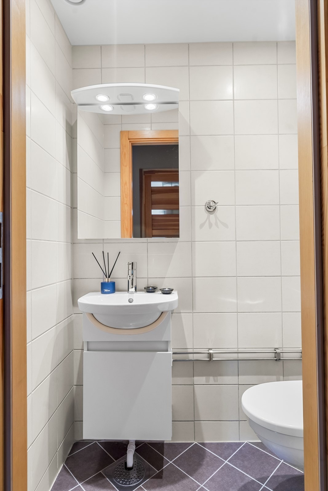 Toalettrommet har flis på gulv og vegger, samt malt overflate og downlights i himling. Det er veggmontert wc, og rommet har naturlig avtrekk. Galleribilde