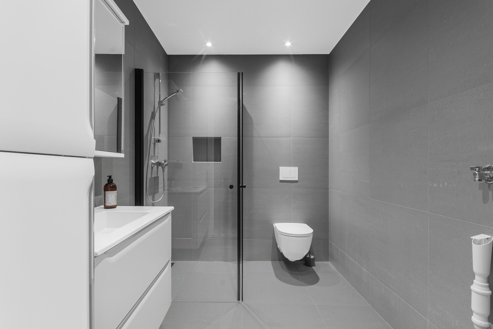 Lekkert og moderne bad med stort dusjhjørne, praktisk vegghengt toalett og opplegg for vaskemaskin.