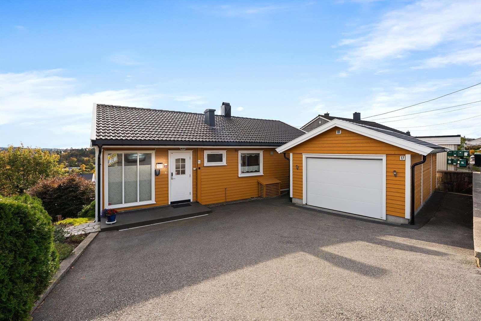 Fra den steinlagte plattingen er det dør direkte inn i garasjen og til passasje bak garasje. Det er også laget en fin gangvei på motsatt side av boligen for enkel tilkomst til hagen. Innkjørselen er praktisk asfaltert med oppsatt el-bil lader i garasje. Galleribilde
