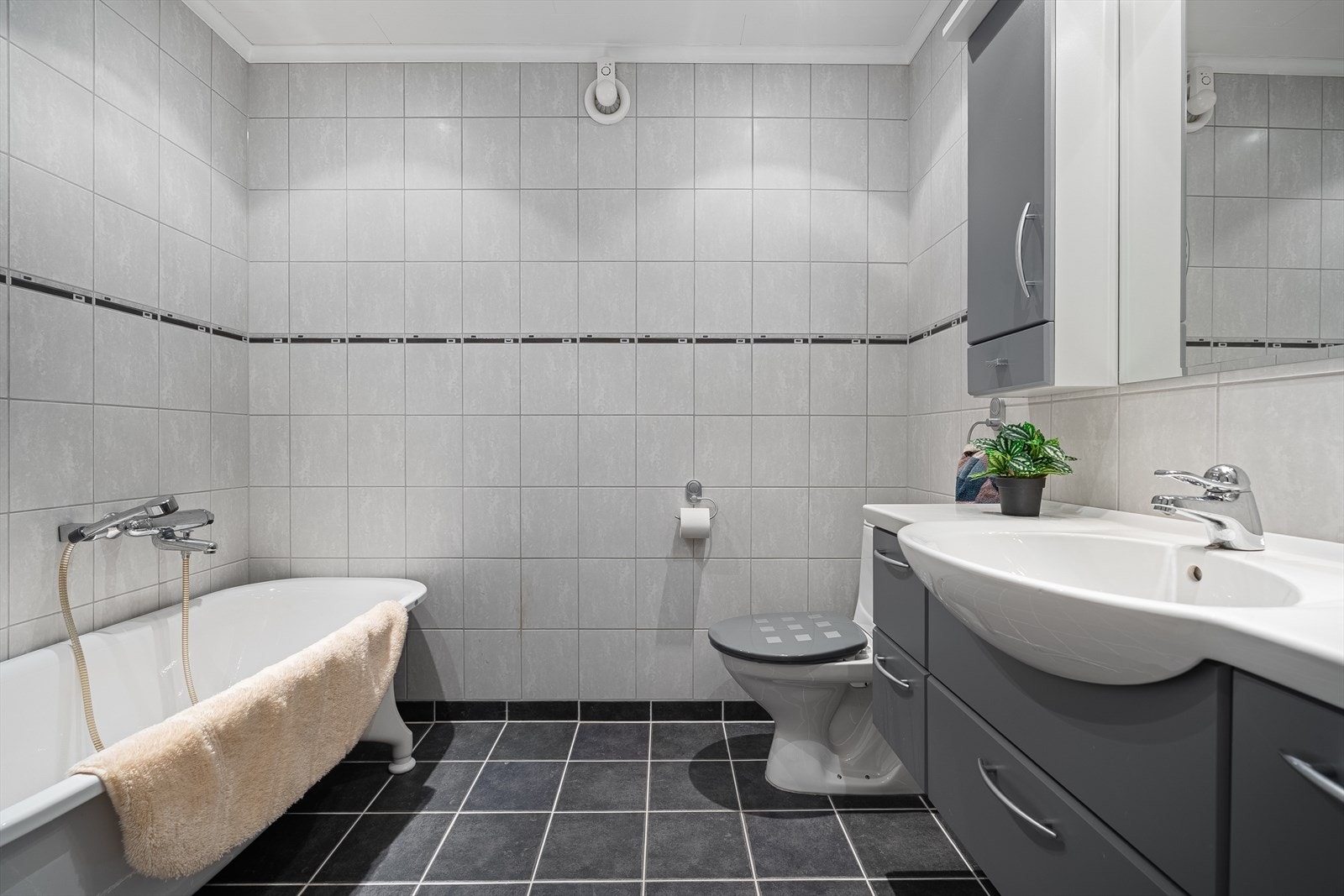 Badet er helfliset med varme i gulvet. Det inneholder et badekar, toalett, samt baderomsinnredning med speil over. Det er downlights i himling, samt elektrisk avtrekk. Galleribilde