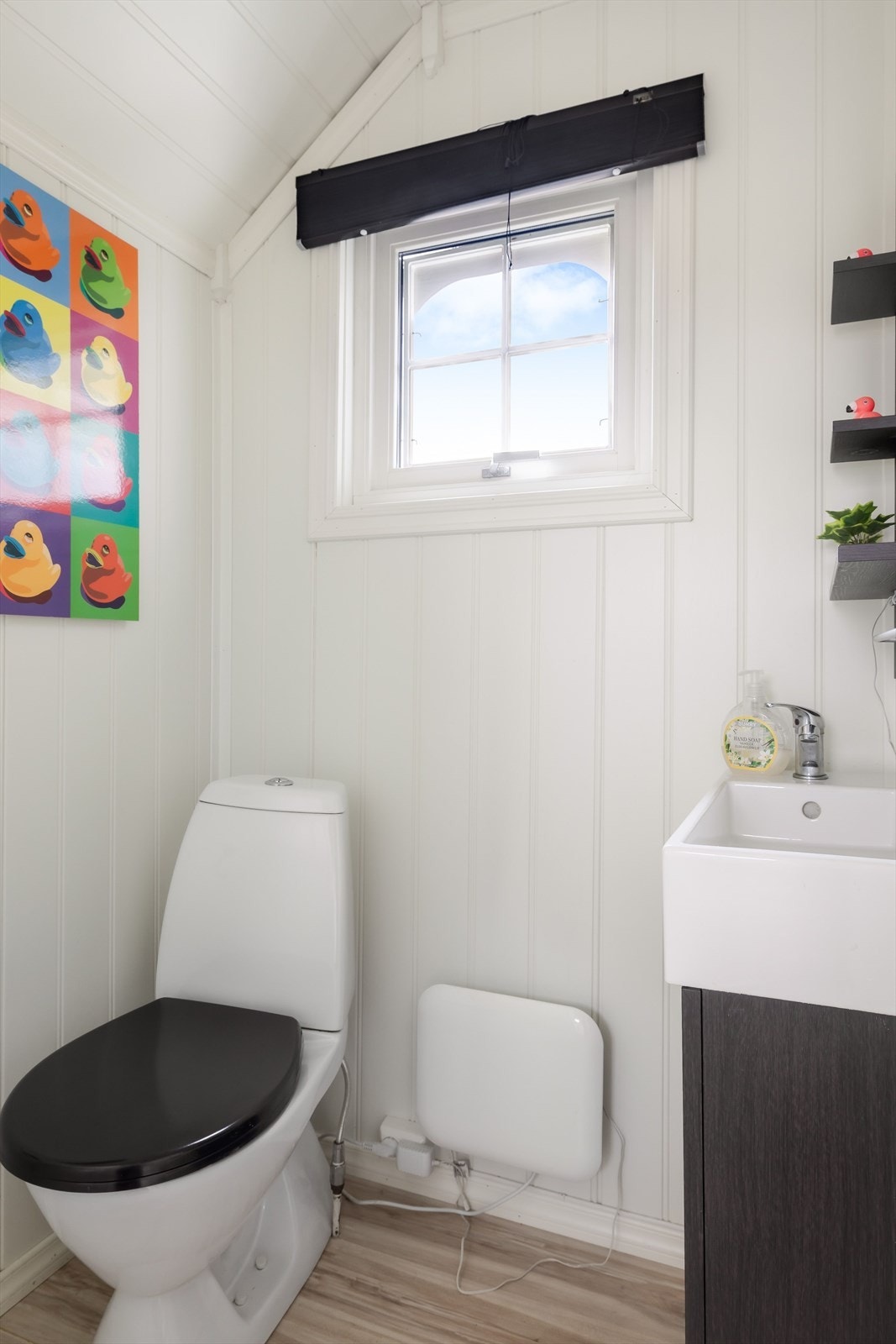 Toalettrom med laminatgulv, panelplater på vegger og panel i himling. Rommet er utstyrt med gulvstående toalett og vegghengt servant. Galleribilde