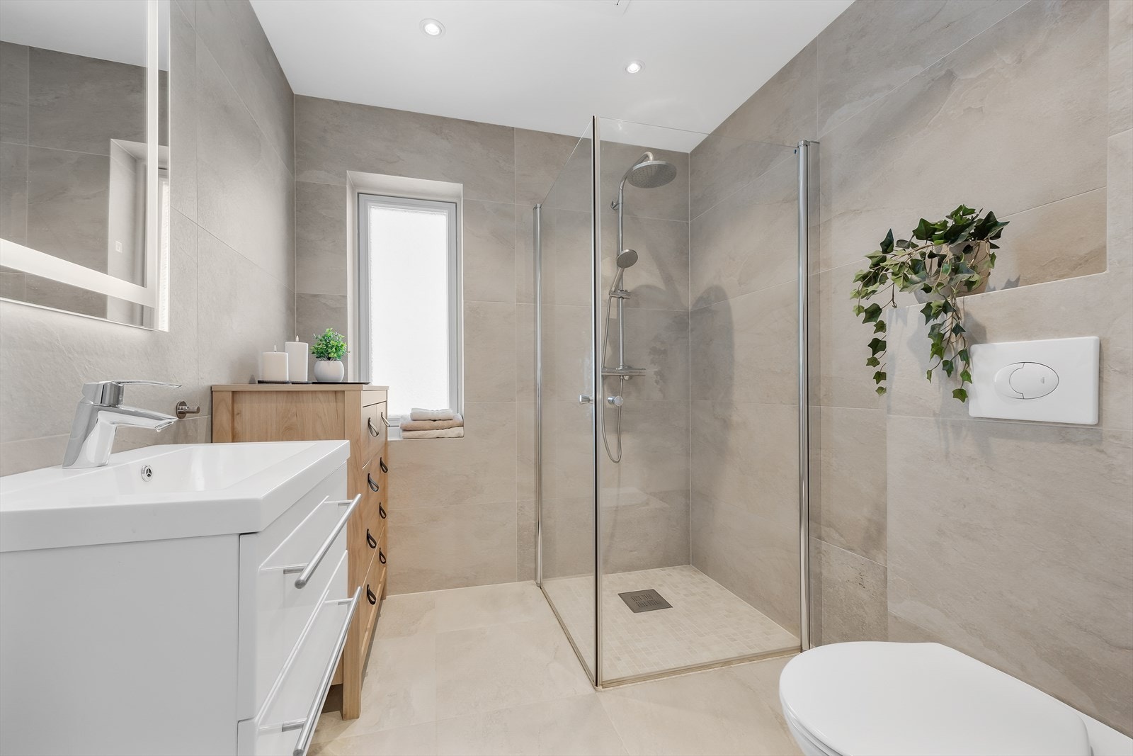 Også badet i andre etasje har gjennomgående lysegrå fliser og varmekabler i gulvet. Galleribilde