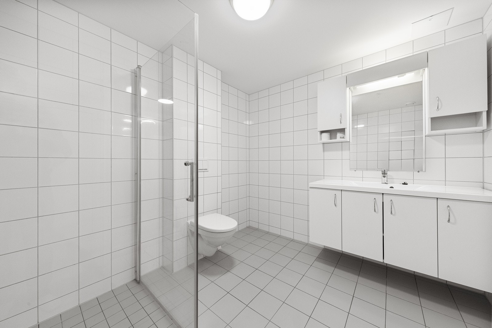 Badet er utstyrt med innredning med heldekkende servant, vegghengt toalett og dusjhjørne med glassdører. Galleribilde