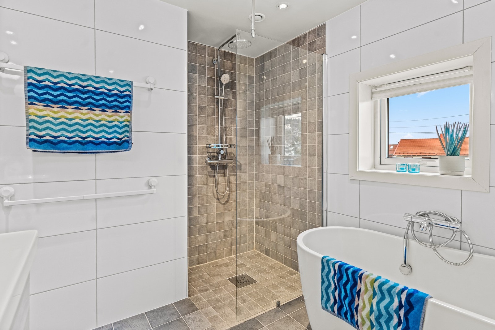 Badet er utstyrt med både dusj på gulv med glassvegg og veggmontert hånd- og regndusj, samt et frittstående badekar med tilhørende armatur. Galleribilde