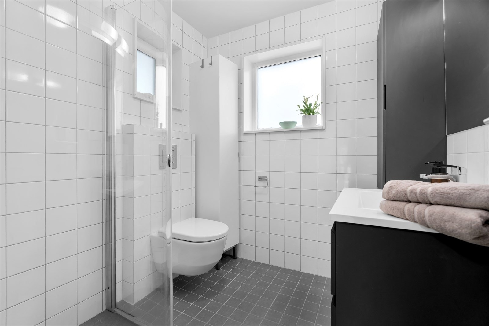Lyst bad med moderne innredning med skuffer, vegghengt WC og dusj med dør og garnityr Galleribilde