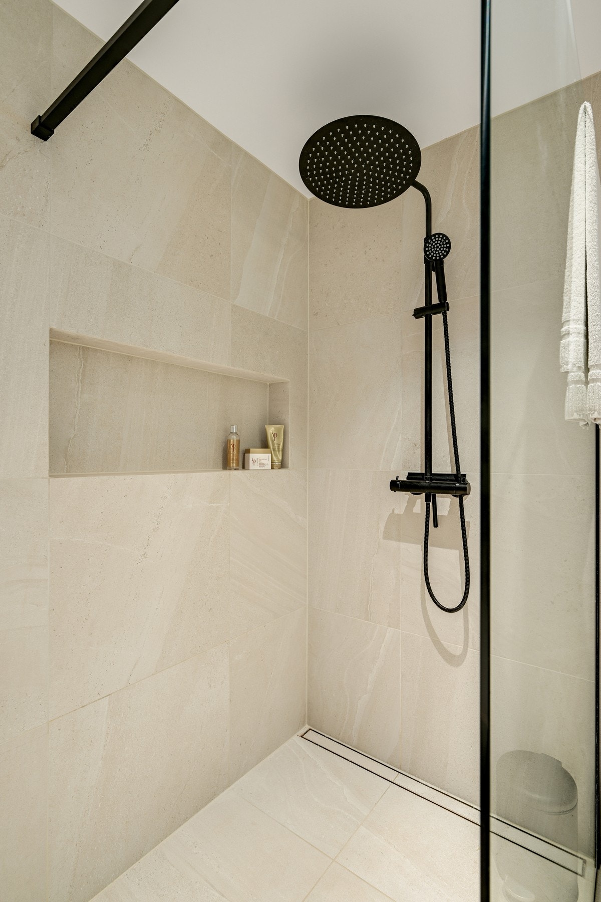 Sorte armaturer og detaljer skaper en stilfull kontrast til de lyse flisene og tilfører badet et eksklusivt, designpreget uttrykk. Galleribilde