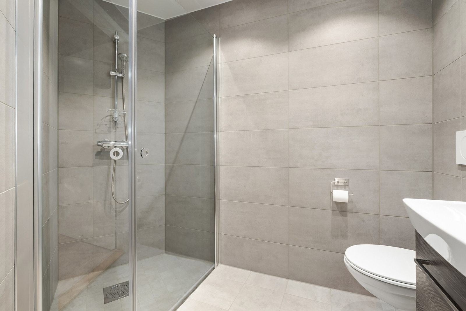 Badet er innredet med vegghengt toalett, dusjhjørne med dusjganityr, og baderomsmøblement med speil og belysning. Galleribilde