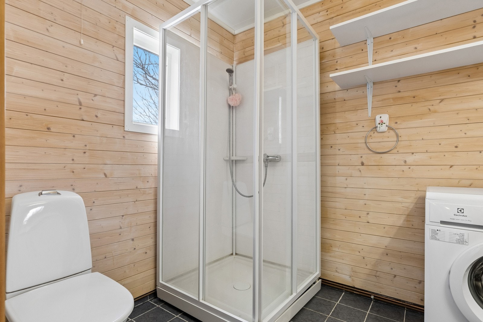 Baderommet har flislagt gulv og dusjkabinett. Opplegg for vaskemaskin.