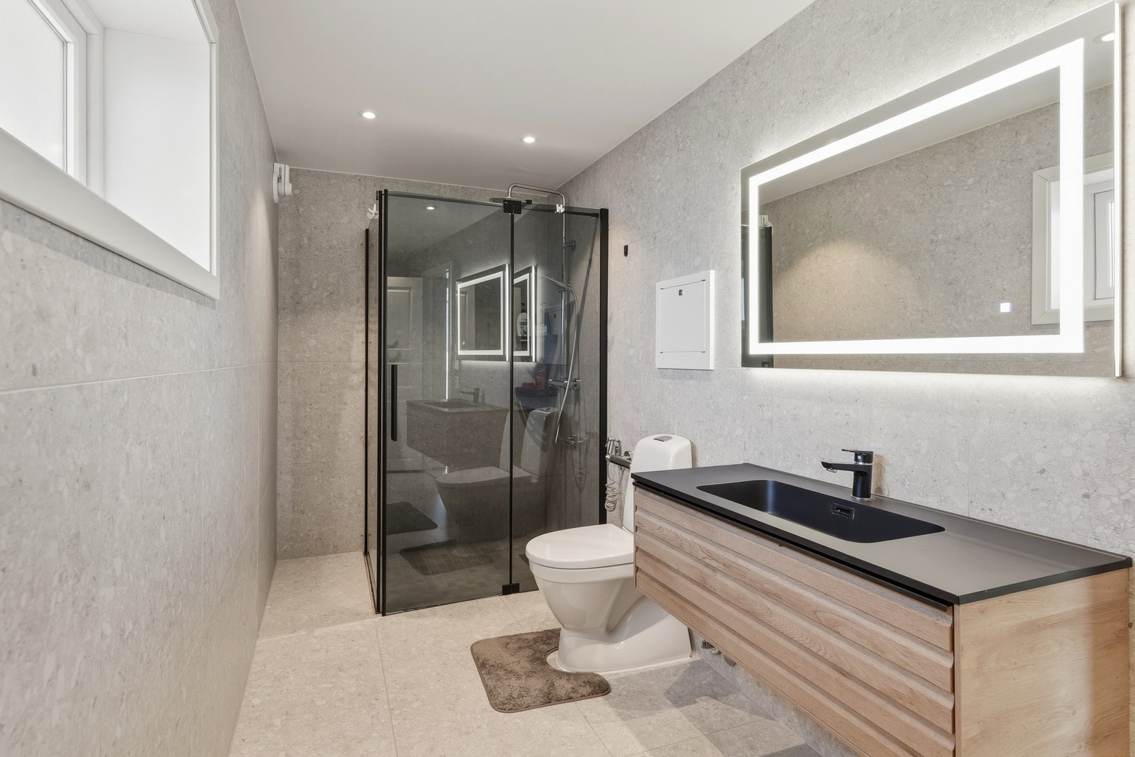 Bad i 1.etg. ble etablert i 2023; et lekkert bad med store, grå fliser i subtilt mønster. Opplegg for vaskemaskin er montert, og badet har toalett, downlights og varmekabler. Galleribilde