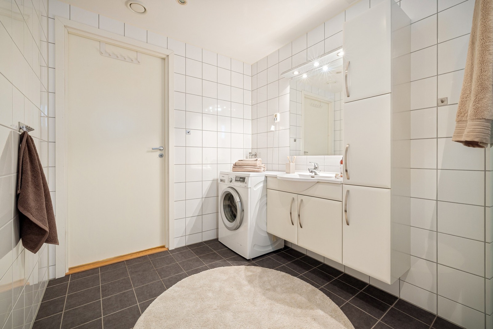 Rommet er innredet med innredning med nedfelt servant, speil, veggmontert toalett og dusjvegger/hjørne, samt opplegg for vaskemaskin. Galleribilde