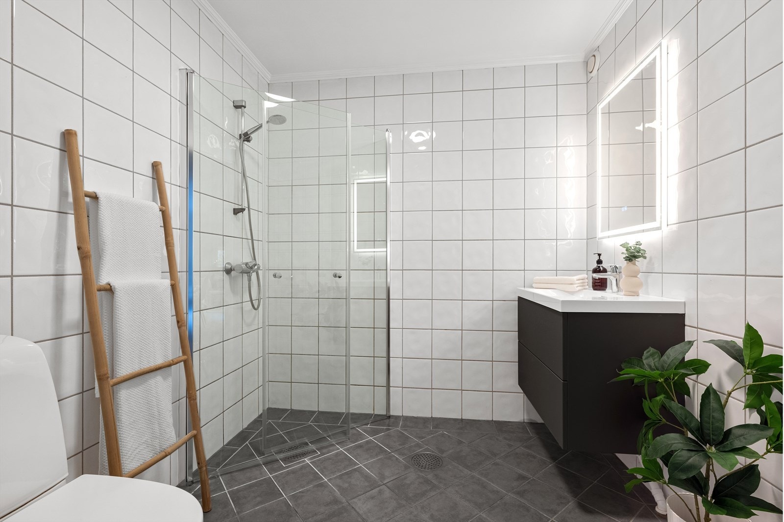 Lys flislagt bad med varme i gulvet. Det er dusjhjørne med innfellbare glassfører, servantskap og speil med belysning. Galleribilde