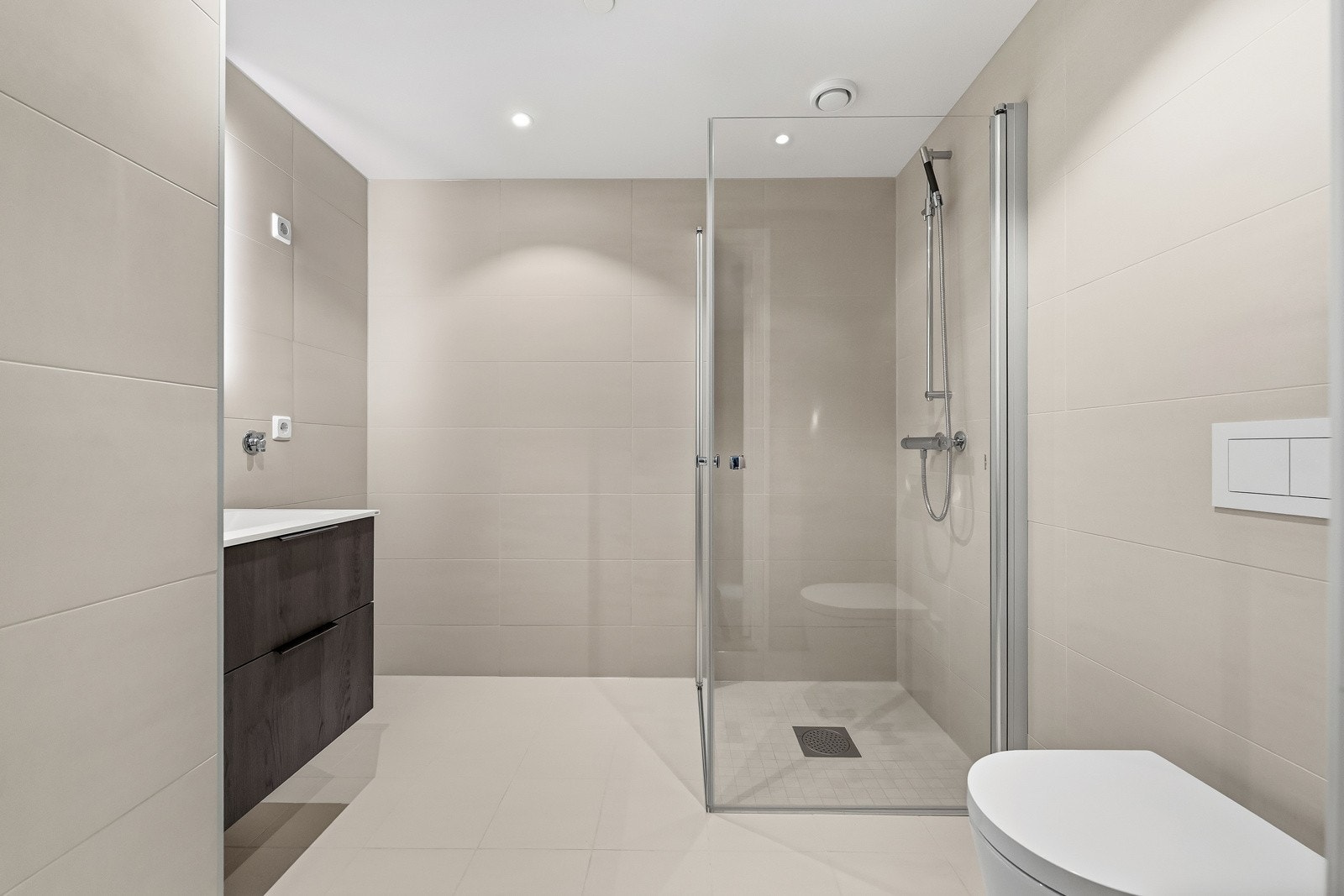 Badet er smakfullt innredet med flislagte vegger og gulv i tidsriktige sandfargede nyanser. Rommet er utstyrt med et praktisk servantskap fra HTH med to skuffer, med fronter som harmonerer med kjøkkenet Galleribilde