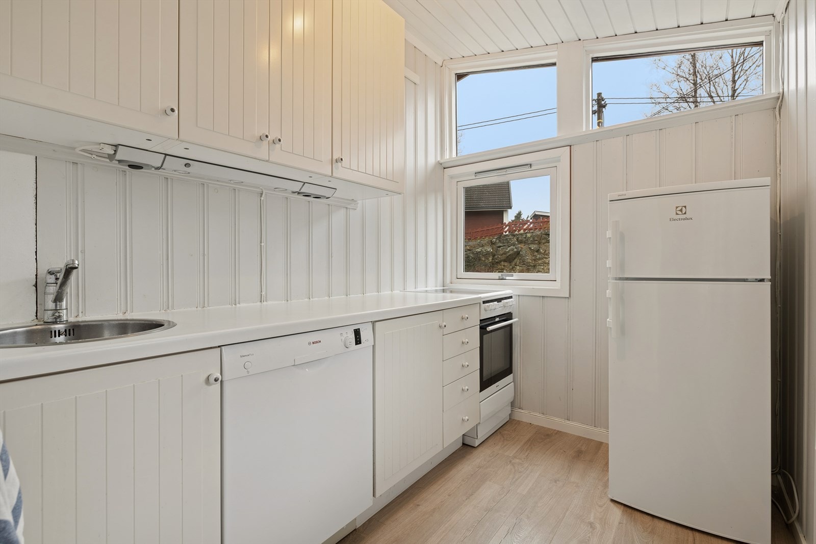 Kjøkkenet er lyst og funksjonelt, med gjennomgående lyse overflater som skaper et rent og innbydende uttrykk. Innredningen består av profilerte, hvite skapfronter og god benkeplass langs én vegg. Galleribilde
