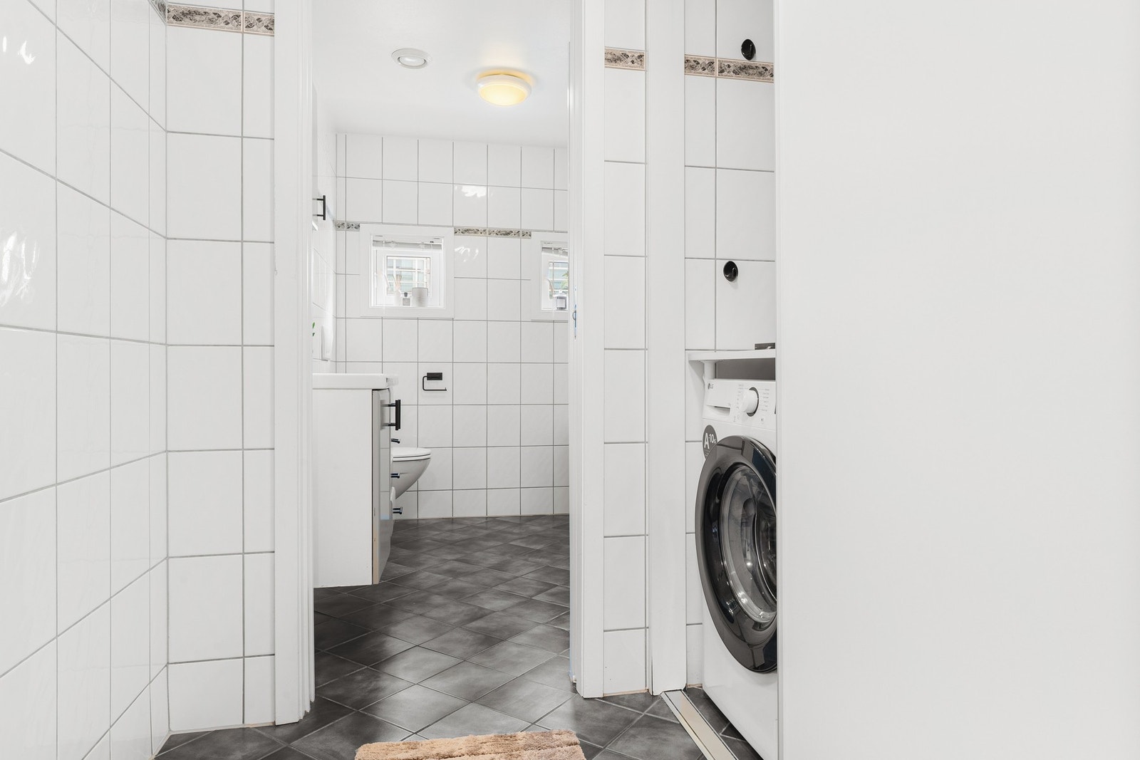 Badet er innredet med dusjhjørne, vegghengt toalett, baderomsinnredning med god skapplass og opplegg for vaskemaskin og tørketrommel. Galleribilde