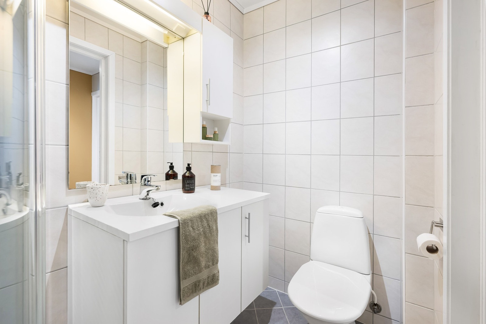 Badet inneholder toalett, helstøpt servant, skap under servant med slette fronter, og dusjdører i klart glass. Det er også opplegg for vaskemaskin. Galleribilde