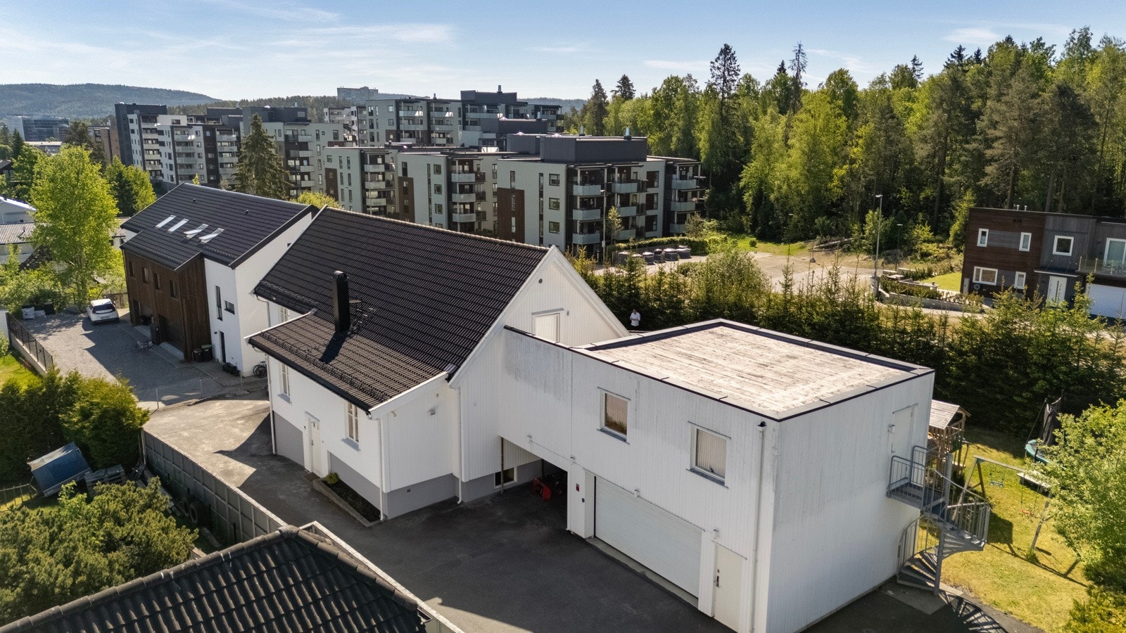 Stor asfaltert gårdsplass med dobbel garasje og carport med lader for elbil. Galleribilde