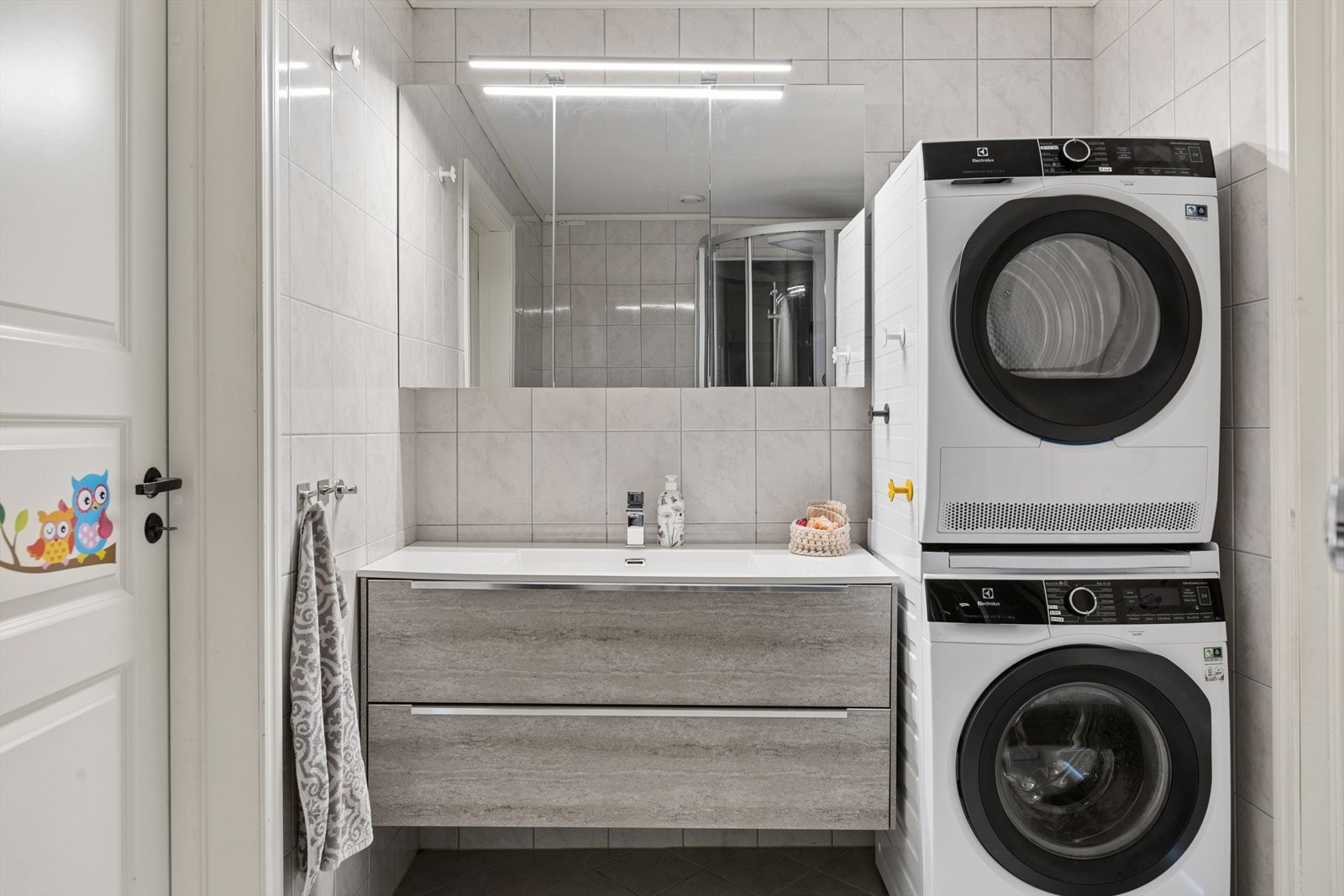Et lyst flislagt bad med moderne baderomsinnreding med heldekkende servant. Romslig speilskap for praktisk oppbevaring. Galleribilde