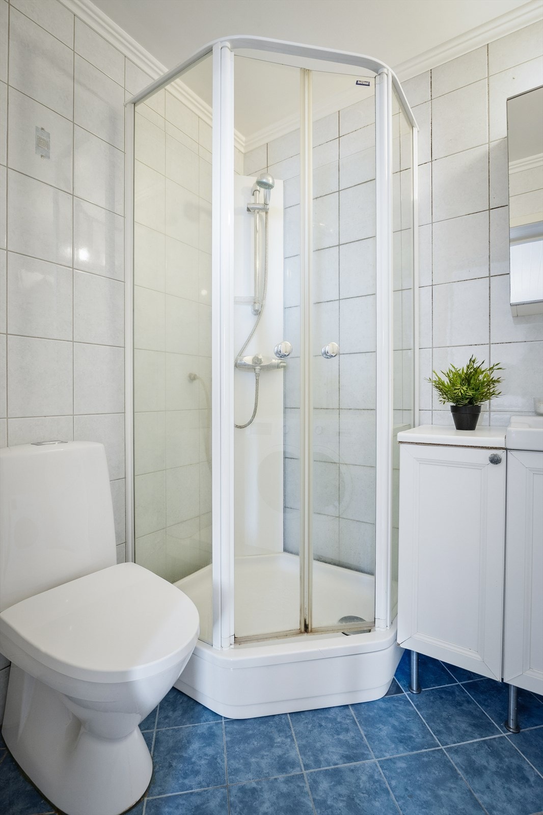 Badet er innredet med gulvstående servantinnredning, speilskap, gulvstående høyskap, dusjkabinett, gulvstående toalett og opplegg for vaskemaskin Galleribilde