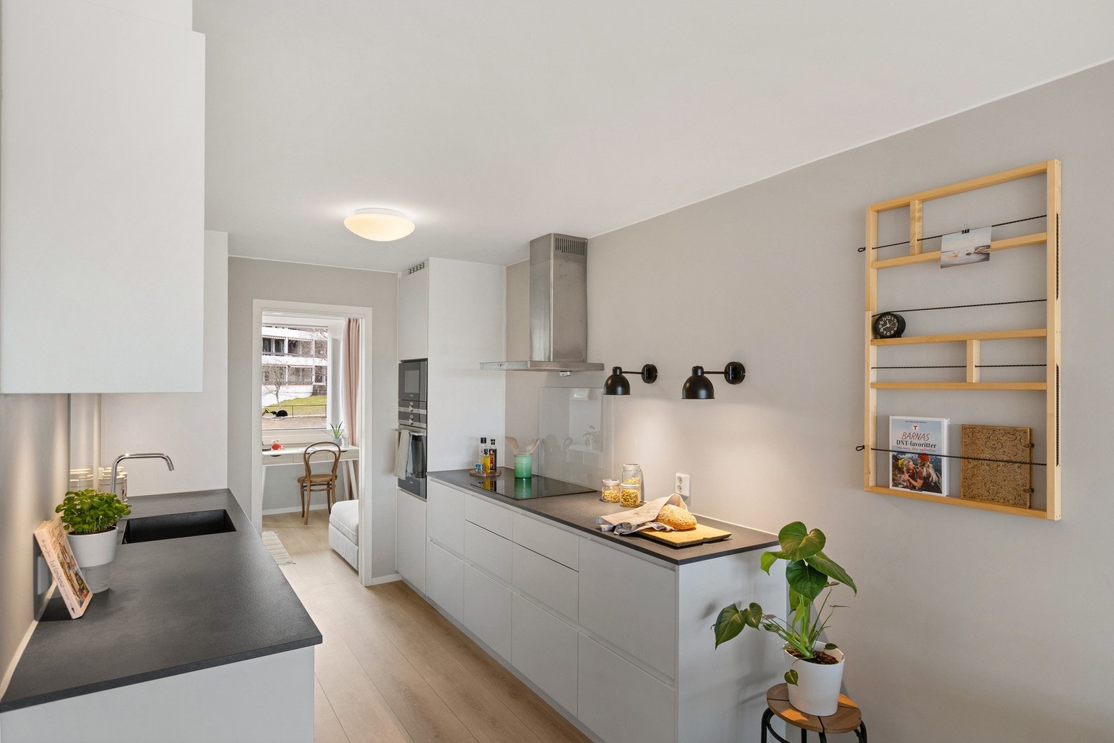 Kjøkken fra Kvik med hvite fronter, mørke benkeflater, integrert kum med stålkran og platetopp med stålventilator. Galleribilde