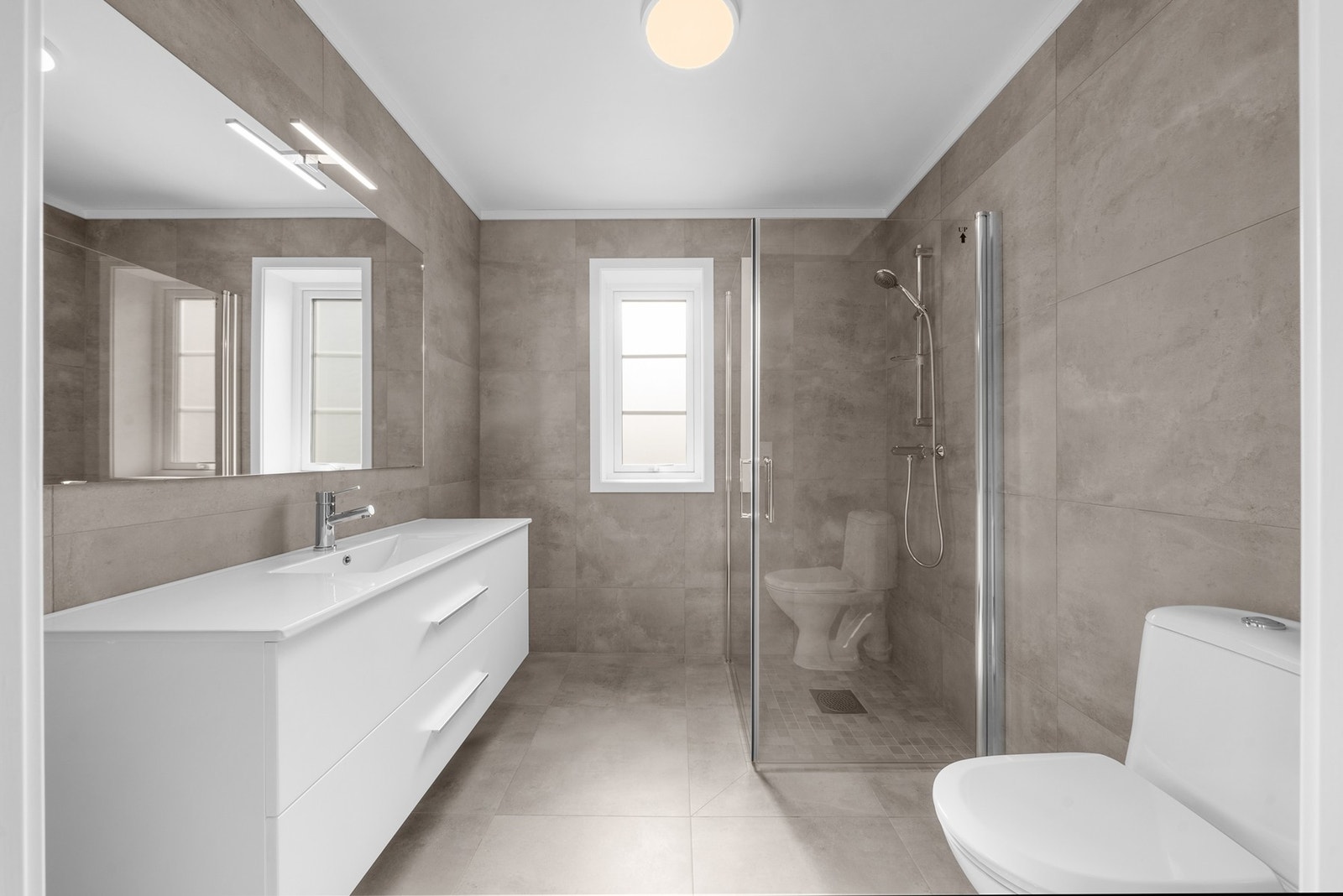 Delikat og moderne bad med flislagte overflater på gulv og vegger. Badet er innredet med dusjnisje med glassvegger, og rommet har vindu som gir mulighet for lufting. Gulvvarme sørger for behagelig komfort året rundt. Galleribilde