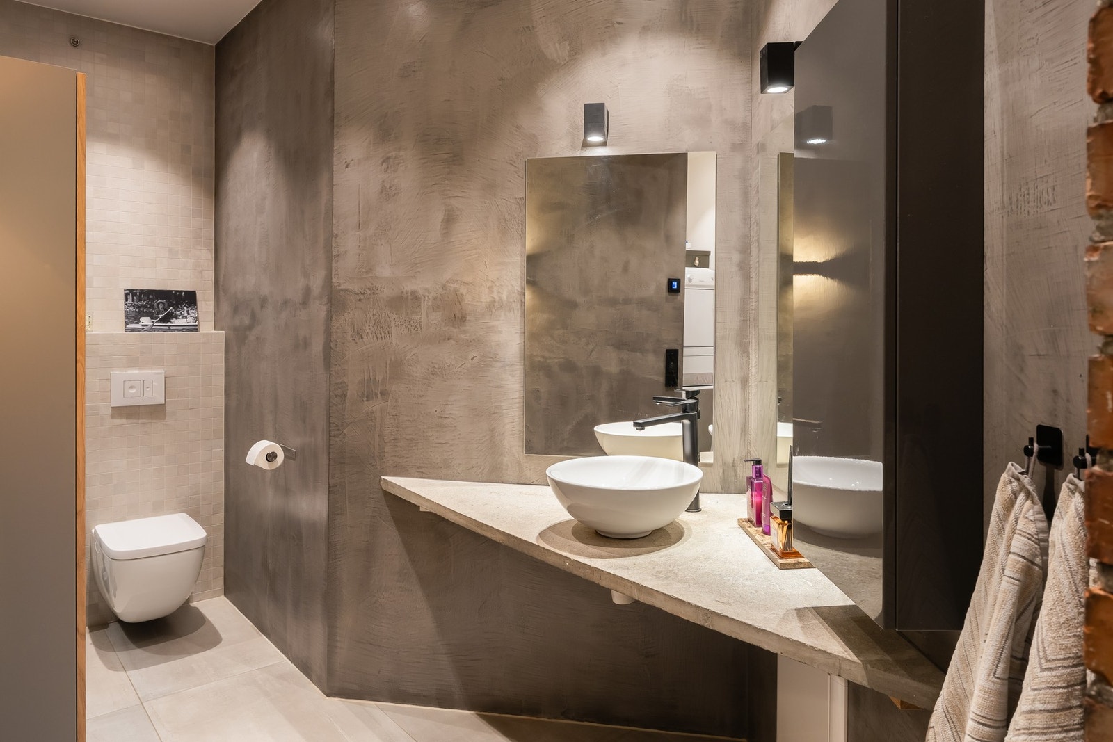 Badet er utstyrt med dusjnisje, vegghengt toalett, egen vaskenisje og servant over betongplate. Galleribilde