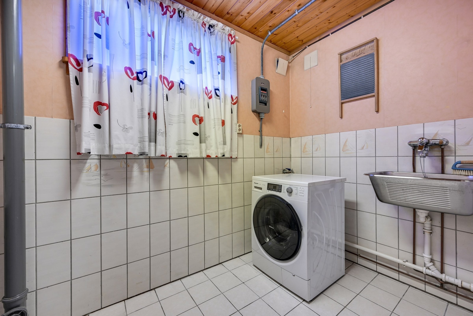 Separat vaskerom i kjelleren med fliser på gulv, skyllekum i stål og opplegg for vaskemaskin. Galleribilde