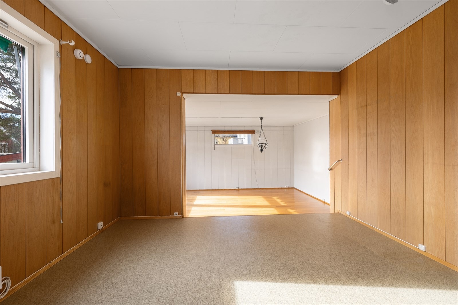 Den ene stuedelen har teppe på gulvet og en vedovn tilkoblet teglsteinspipe. Galleribilde