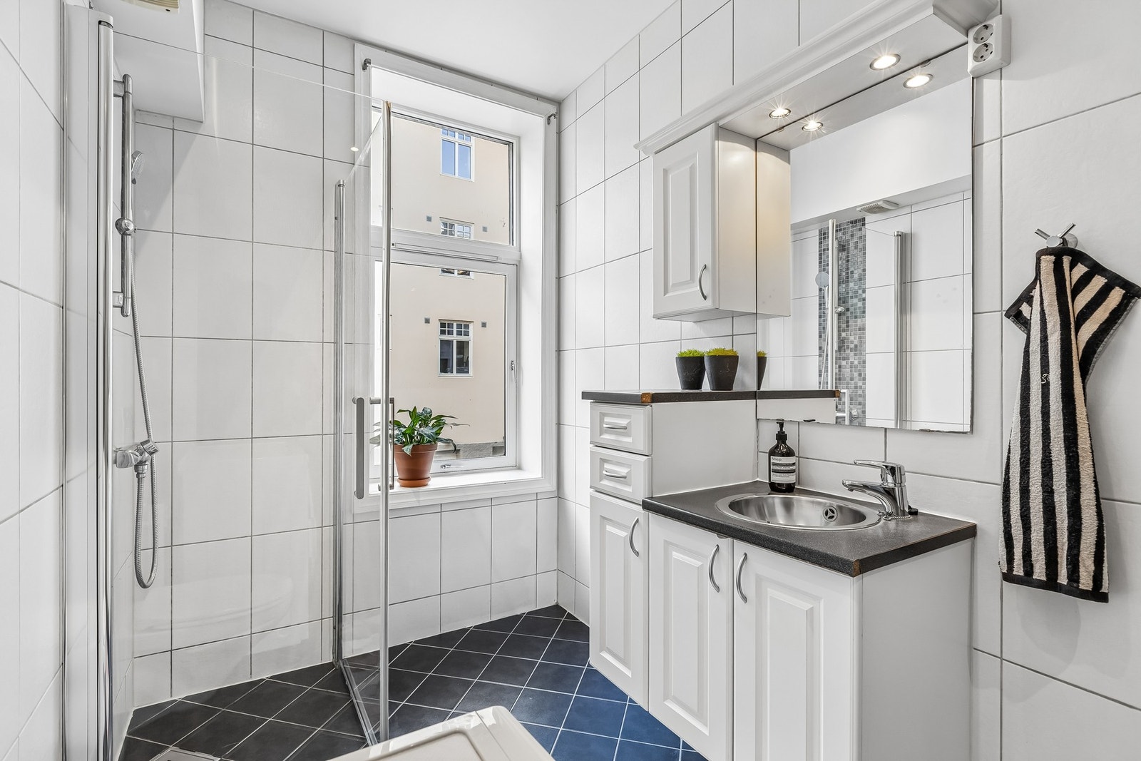 Badet er innredet med vegghengt servantinnredning, speil med lys, dusjhjørne med dører og vegghengt toalett. Galleribilde