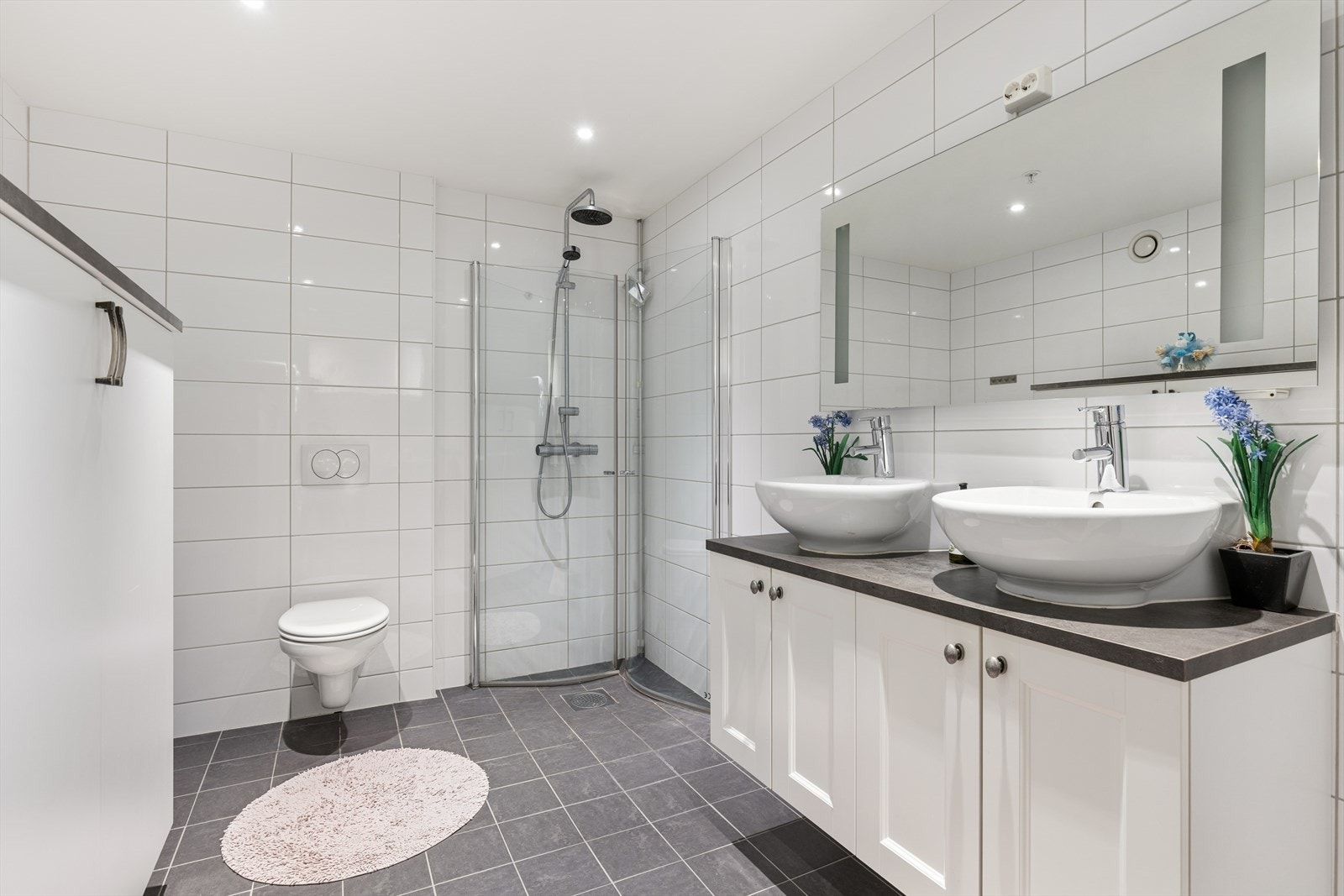 Bad / vaskerom. Badet er utstyrt ved vegg hengt toalett. dusjnisje speil med belysning, servant med oppbevaring under. Galleribilde