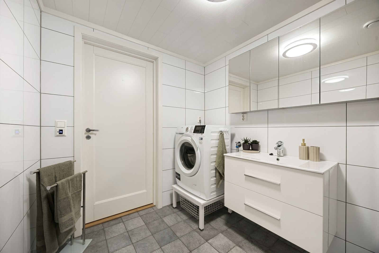 Badet inneholder heldekkende servant med underskap, overskap med speilfronter, gulvmontert toalett, dusjnisje og opplegg til vaskemaskin. Galleribilde
