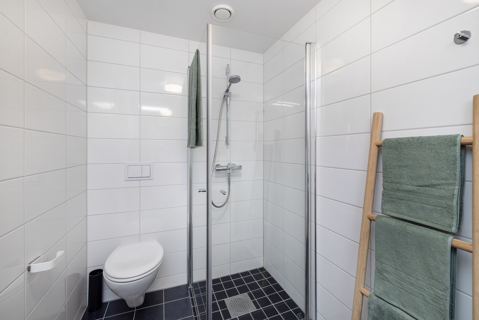 Badet er flislagt og utstyrt med vegghengt toalett og et dusjhjørne med glassdører. Galleribilde