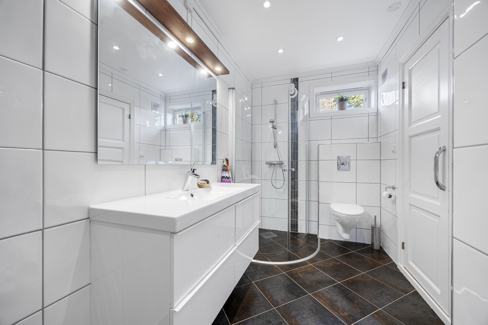 Badet i underetasjen har fliser på gulv og vegger, og er utstyrt med dusjvegger, toalett og en servant nedfelt i innredningen. Galleribilde