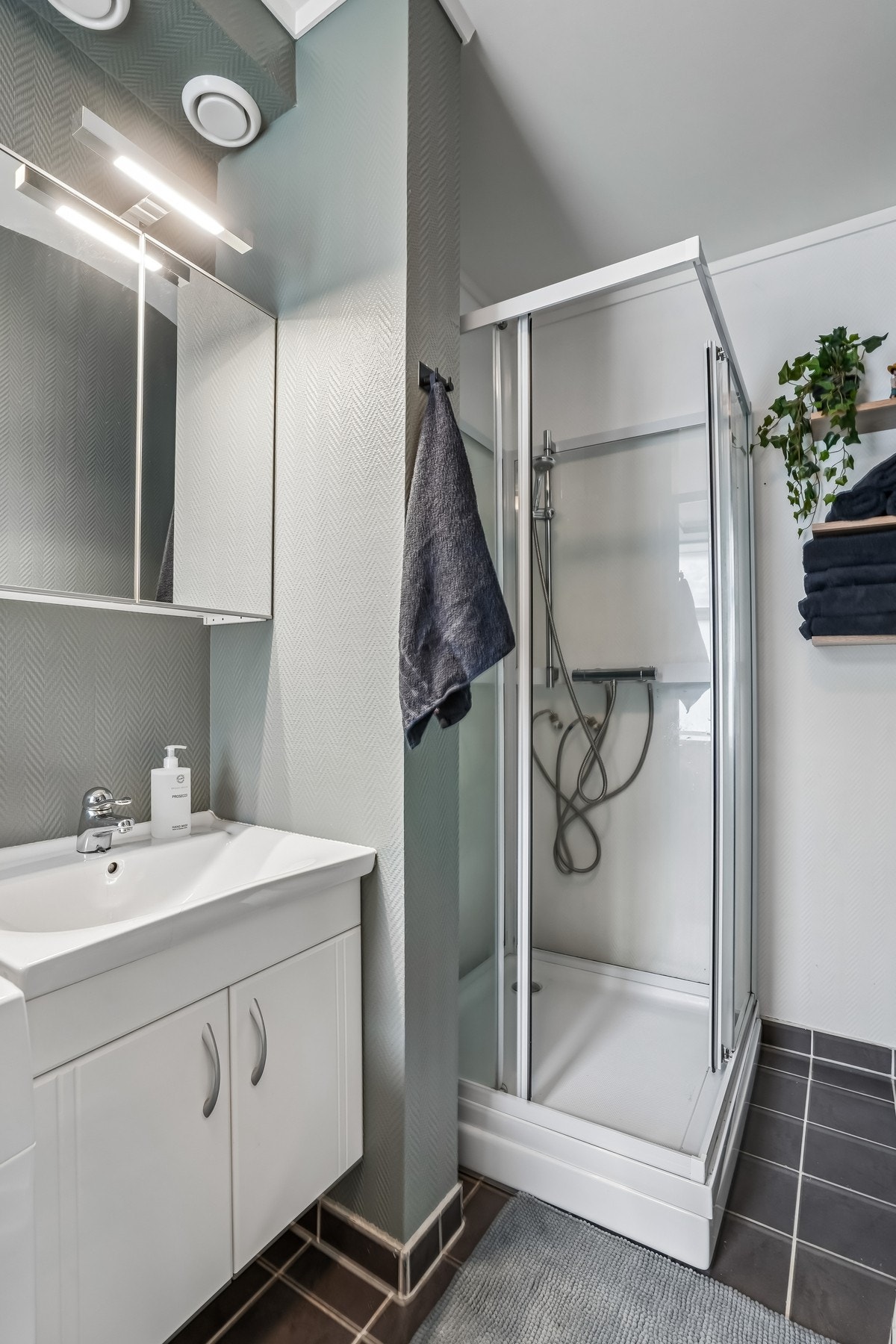 Badet er utstyrt med toalett, dusjkabinett og baderomsmøbel med overliggende speilskap med belysning. Galleribilde