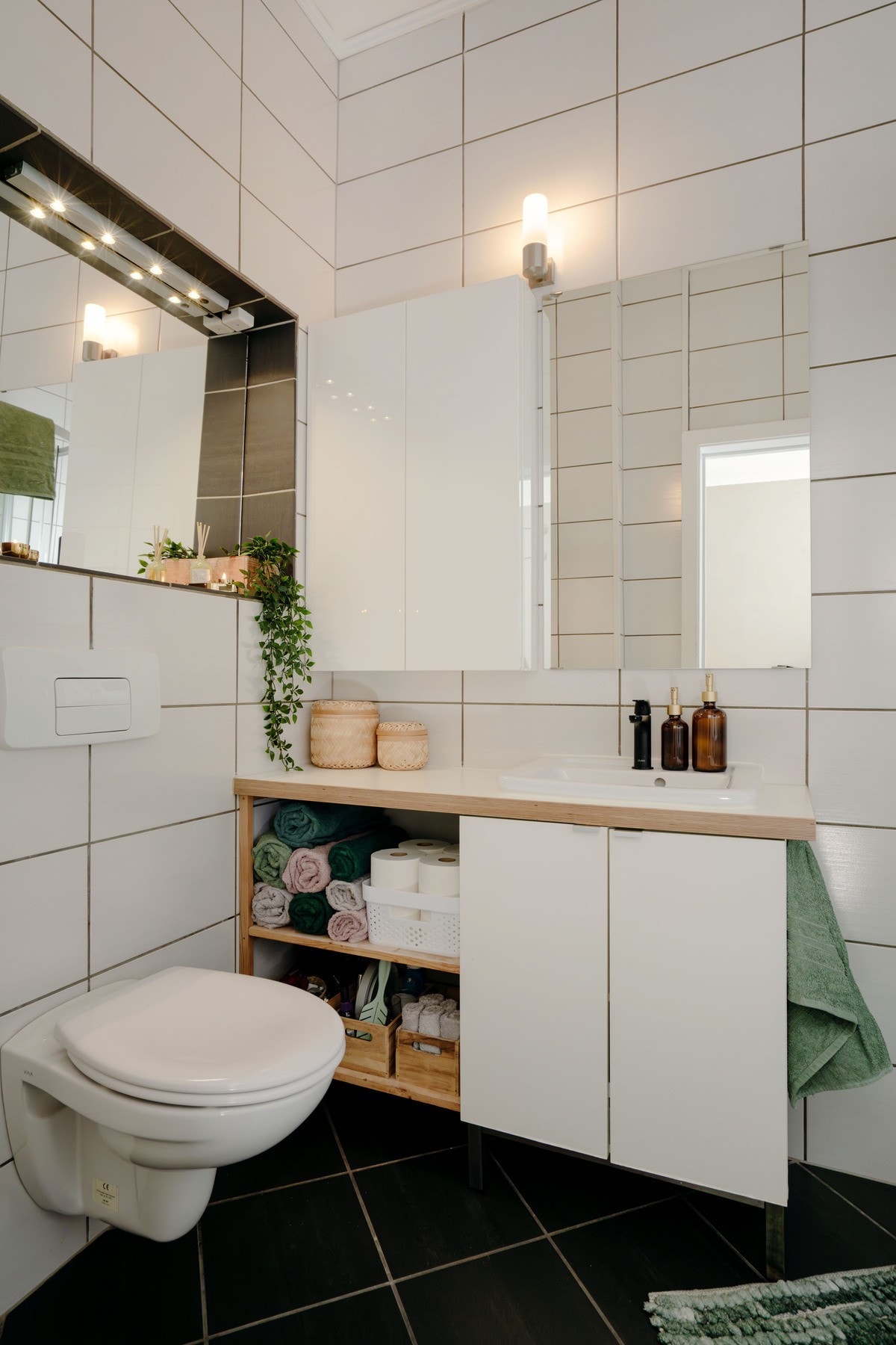 Badet er flislagt med vegghengt toalett, servant med hyller og skap Galleribilde