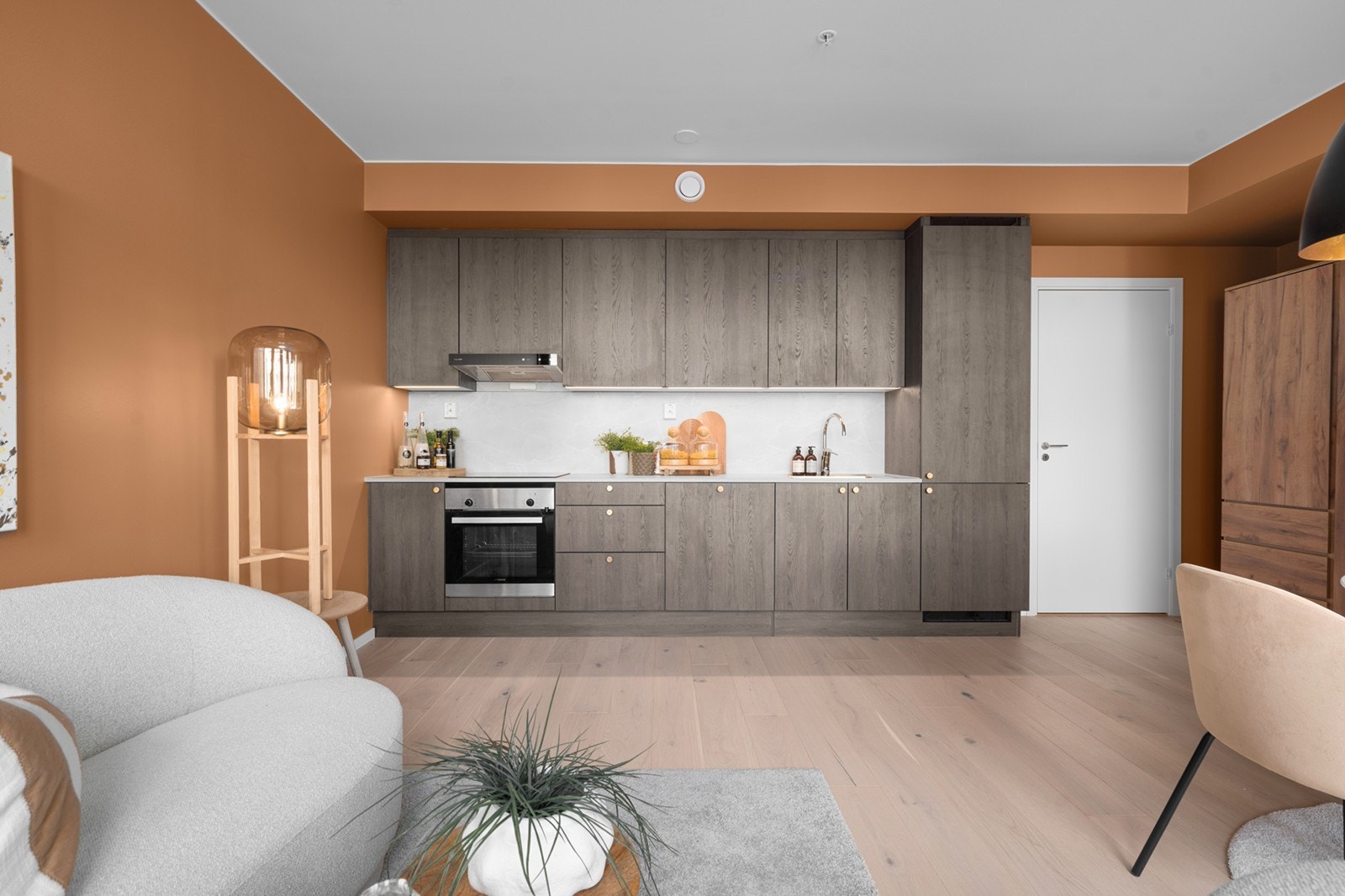 Kjøkkenet fremstår som moderne og stilrent med en helhetlig innredning i delikate, jordnære toner. Slette fronter i en lun trestruktur kombineres med en lys benkeplate og integrerte løsninger, som gir et ryddig og tidsriktig uttrykk Galleribilde