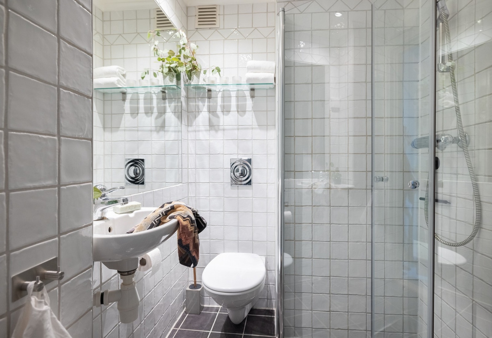 Delikat, flislagt bad med en praktisk og funksjonell utforming. Badet er innredet med servant, vegghengt toalett og dusjhjørne med glassvegger. Galleribilde