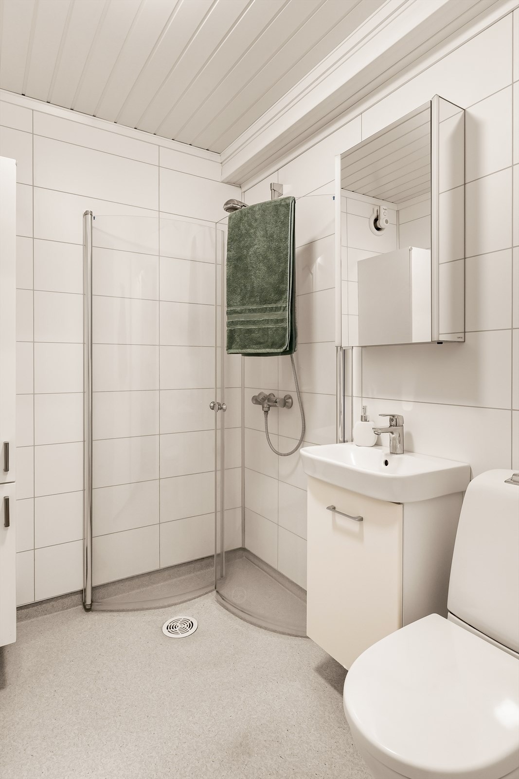 Badet er utstyrt med en pen innredning med nedfelt servant, toalett og et romslig dusjhjørne med glassdører, som gir et ryddig og moderne preg.
Videre har rommet speilskap og høyskap som gir gode oppbevaringsmuligheter. Galleribilde