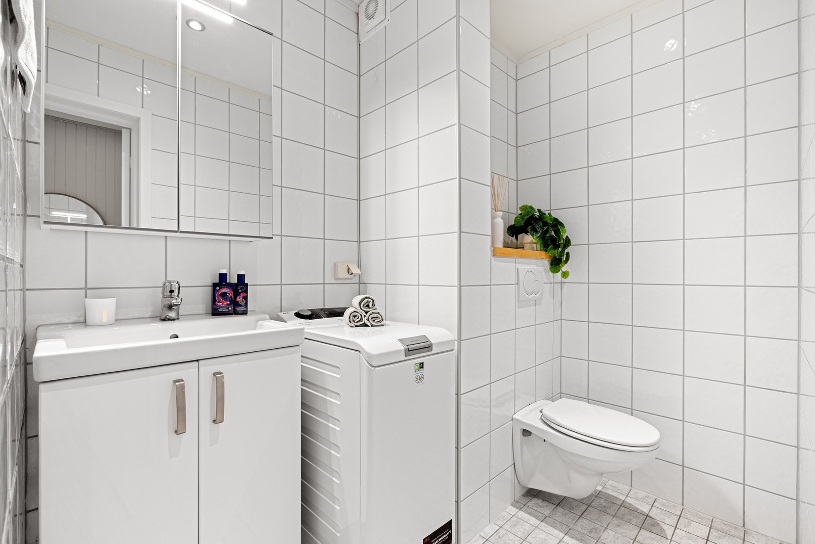 Badet er innredet med vegghengt WC, dusjhjørne, servant på underskap og speil. Rommet belyses av downlights i himling. Galleribilde