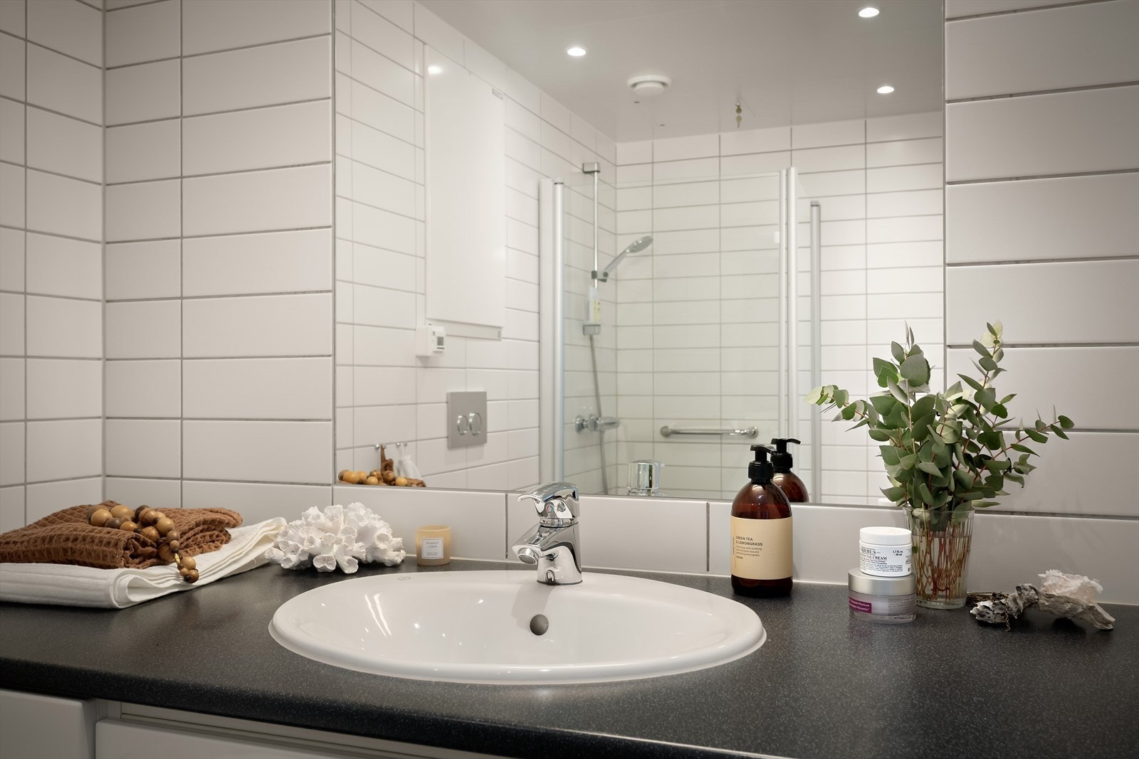 Badet er utstyrt med en slett, lys innredning med servant, innmurt speil med lys over, og et veggmontert toalett. Det er en dusjnisje med innfellbare dører i glass, samt opplegg for vaskemaskin. Galleribilde