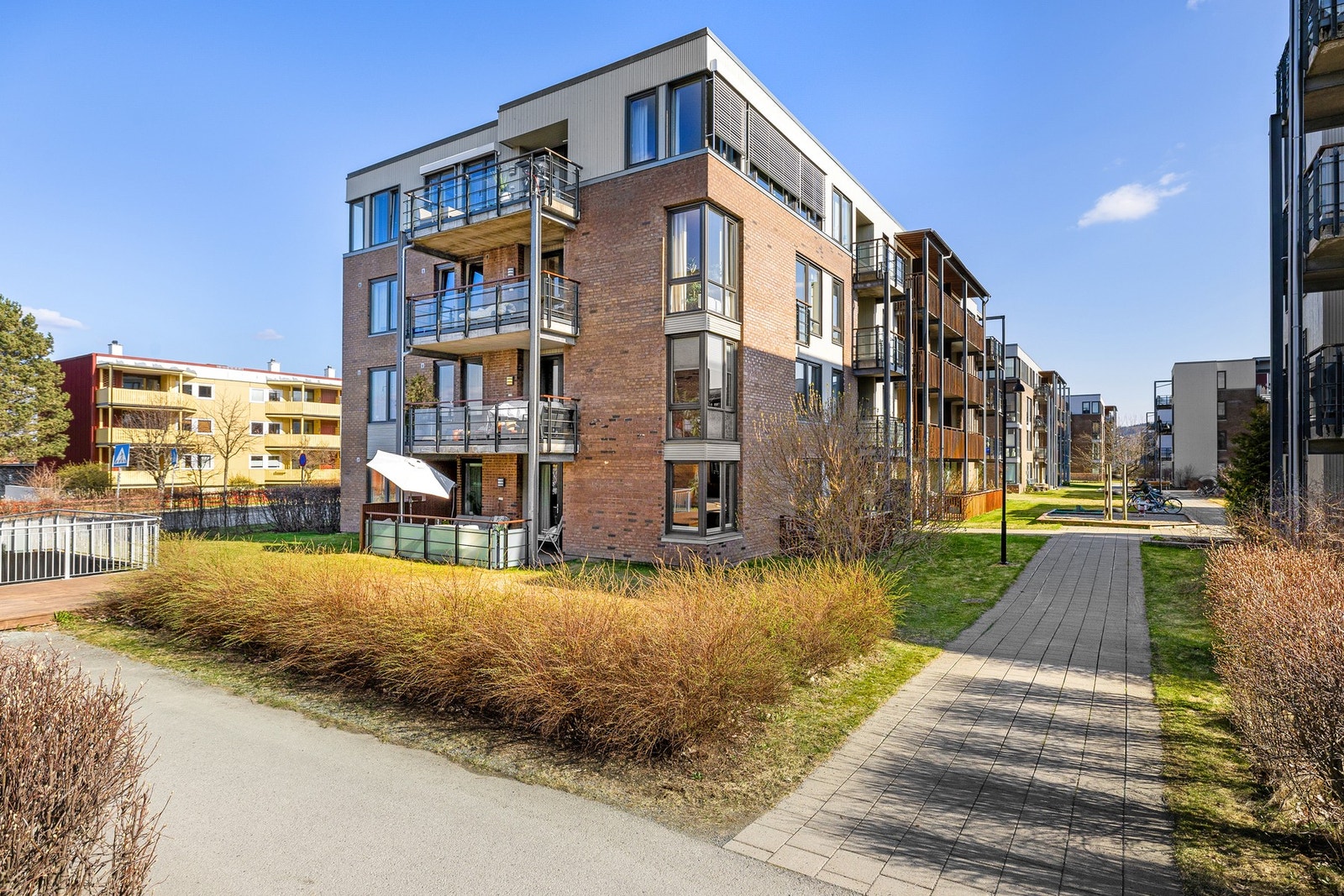 Fasadebilde. Mellom og rundt blokkene har du pene utearealer. Oppleves grønt og frodig på sommerhalvåret. Galleribilde