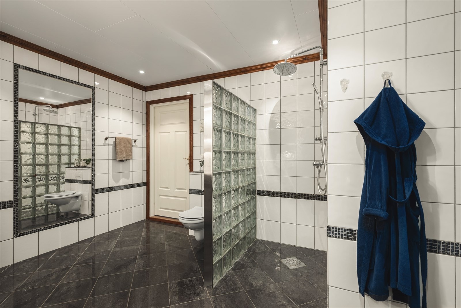 Badet er innredet med pen baderomsinnredning, veggmontert toalett og dusjnisje med vegg av glassbyggerstein Galleribilde