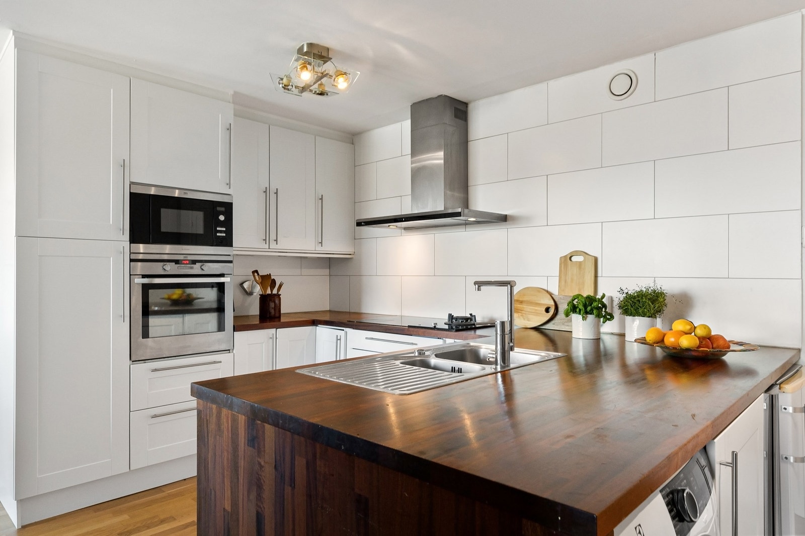 Pent kjøkken med profilerte fronter på skap og skuffer, og benkeplate av tre med dobbel oppvaskkum Galleribilde