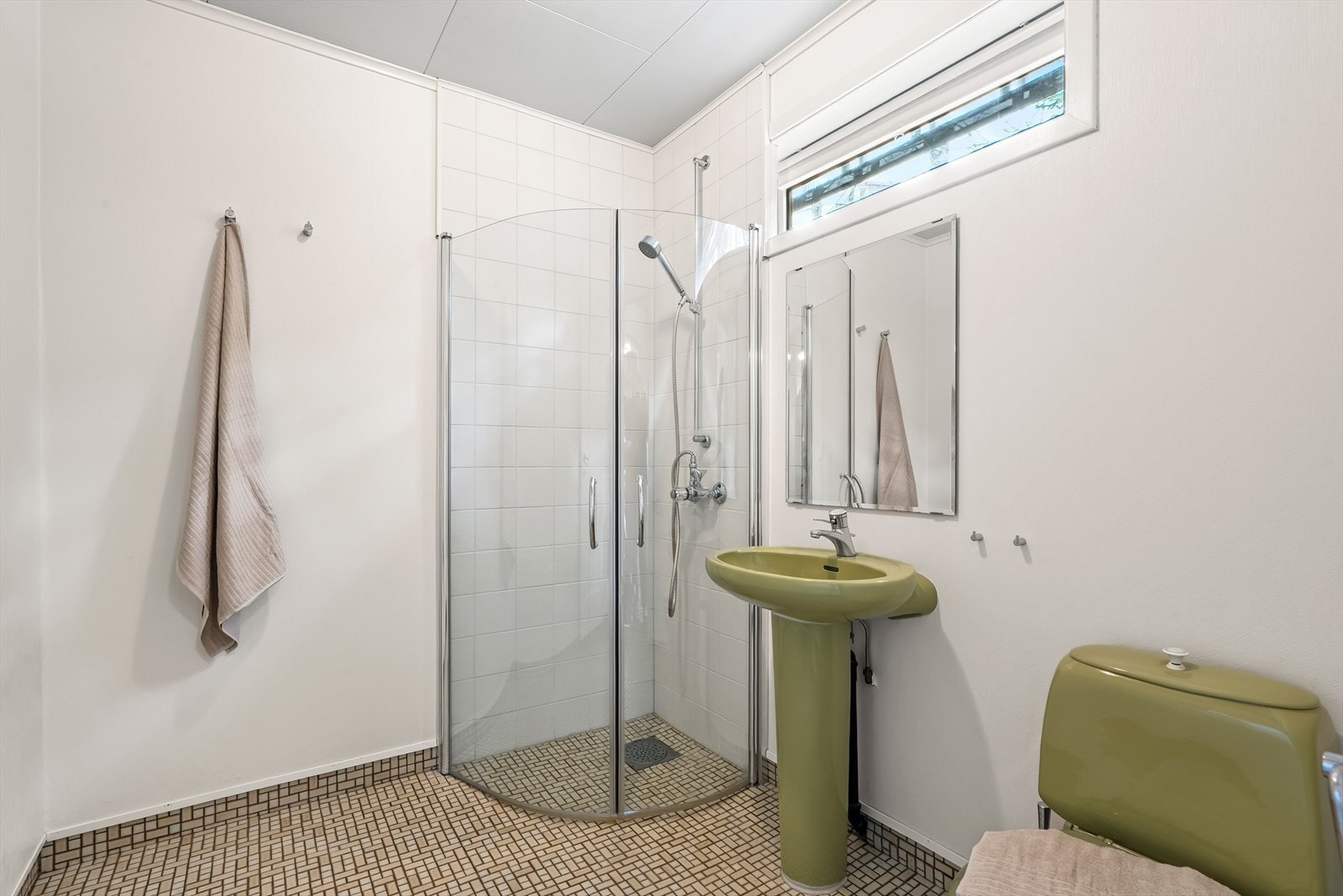 Bad i underetasje med flislagt gulv og elektriske varmekabler. Badet er innredet med toalett, vegghengt servant og dusjhjørne med innfellbare glassdører Galleribilde